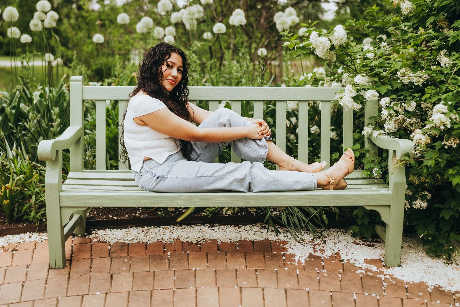 Someone lounges peacefully on a white garden bench surrounded by blooming white flowers in a tranquil outdoor setting.