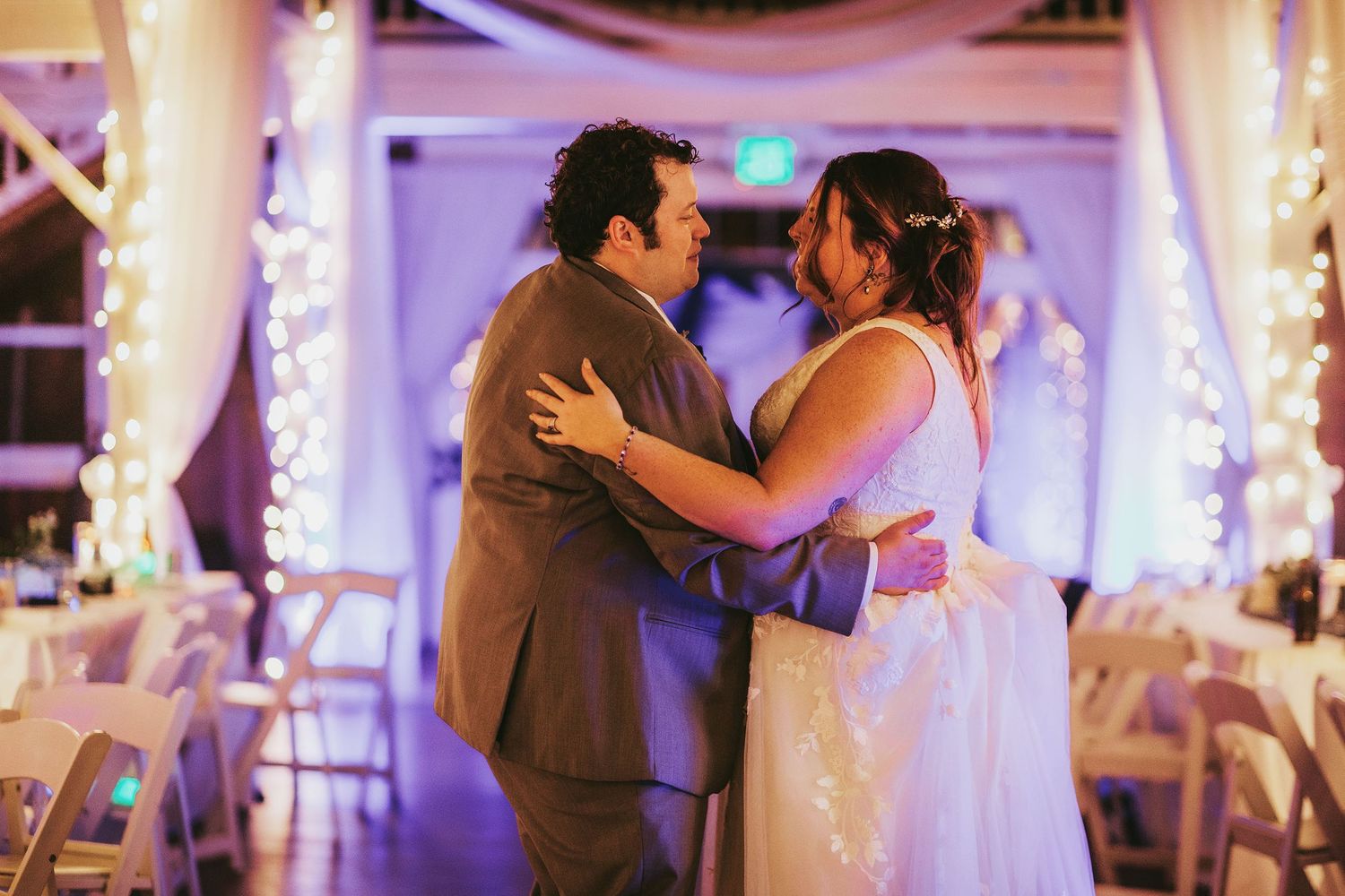 Romantic first dance at a wedding reception with purple uplighting and white draping decorations.