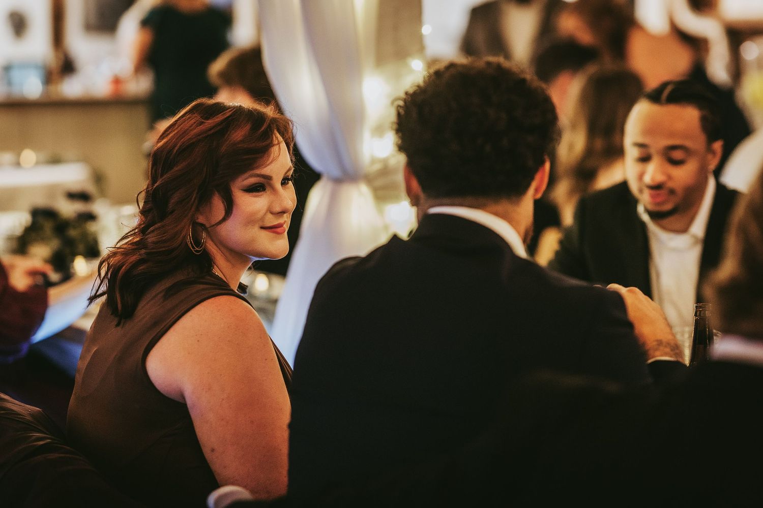 Wedding reception celebration with guests mingling in warm ambient lighting.