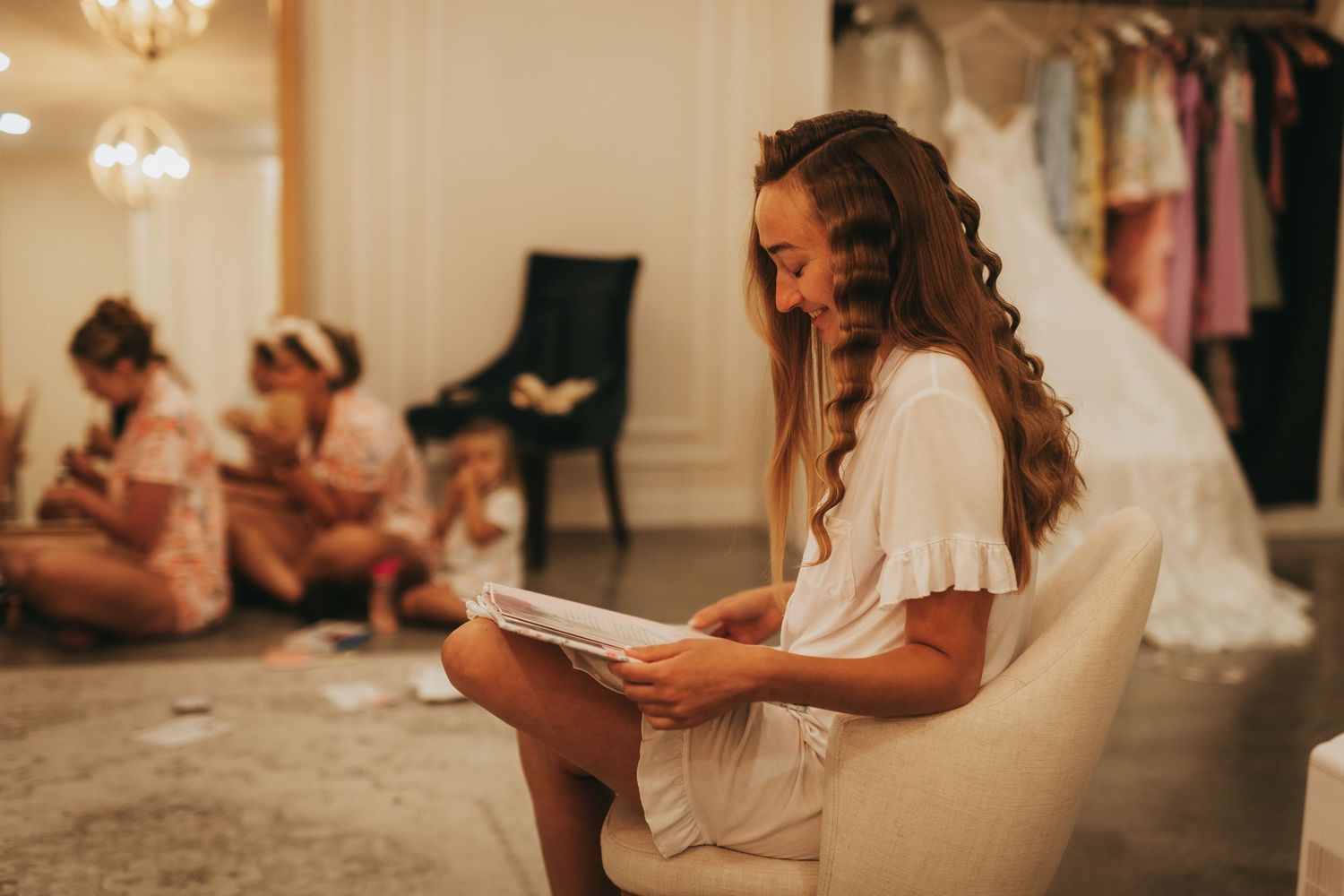 Bride reading a note while bridesmaids get ready in background.