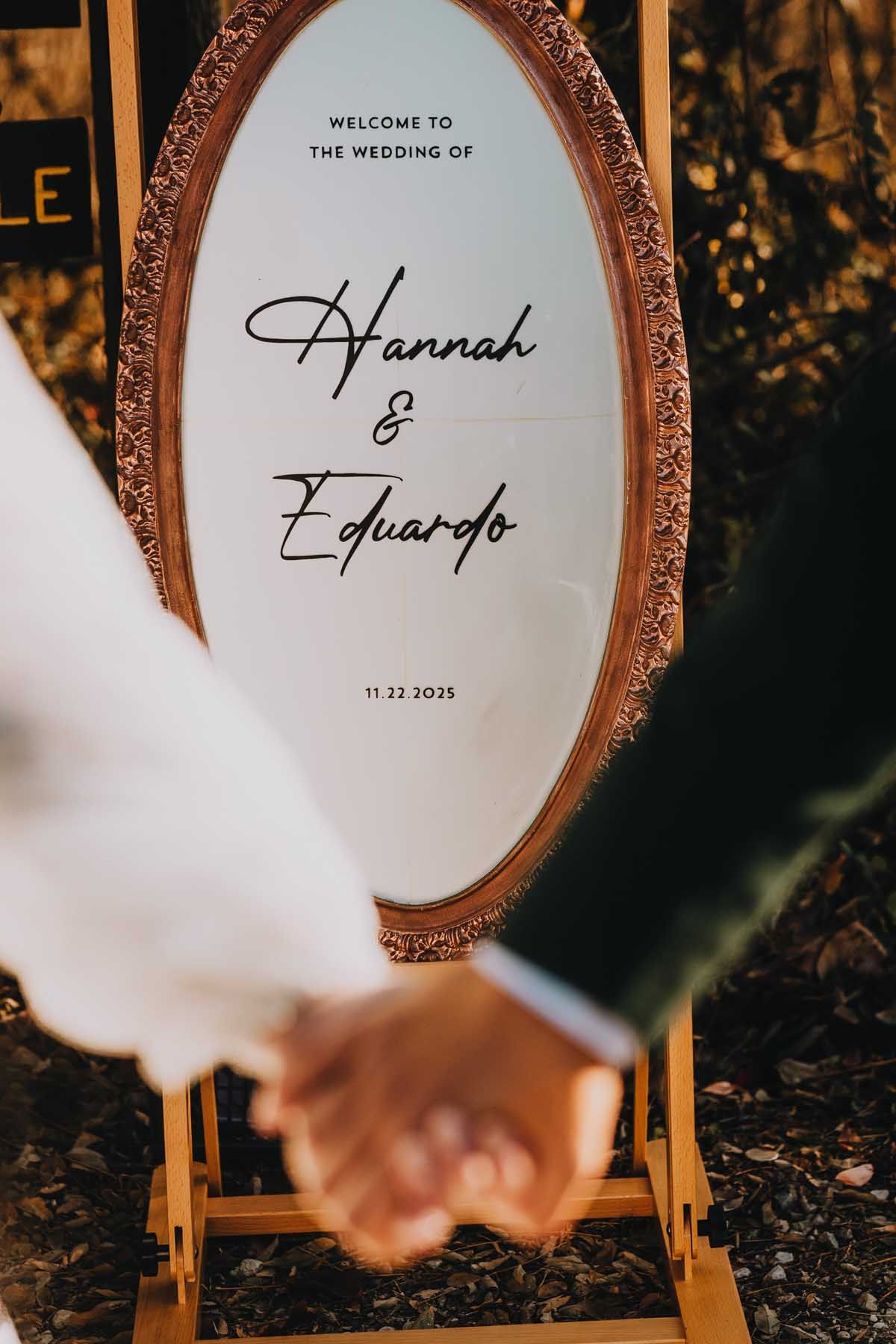 Elegant framed wedding welcome sign with calligraphy text displayed outdoors against a dark background.