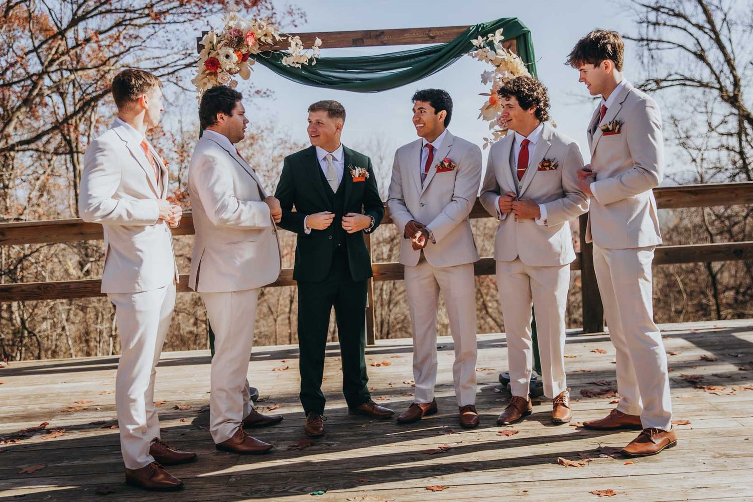 Wedding party members in white suits and dark jackets gather outdoors during a sunny celebration.