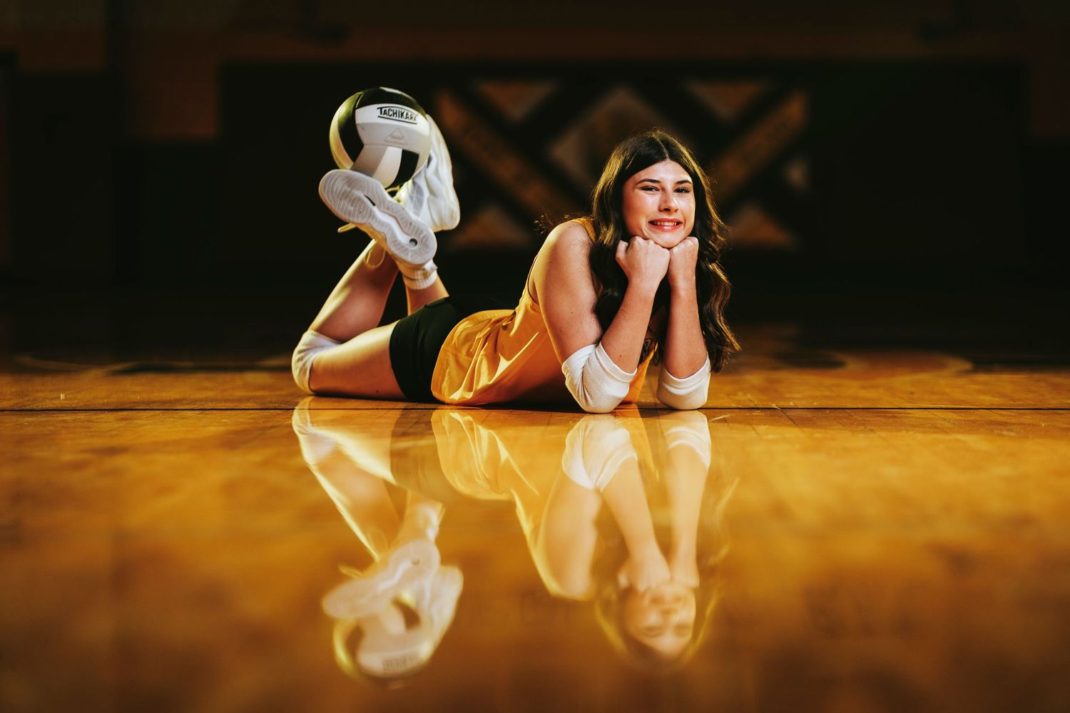 A graceful ballet dancer in a flowing white dress performs an elegant pose on a wooden stage floor in warm lighting.