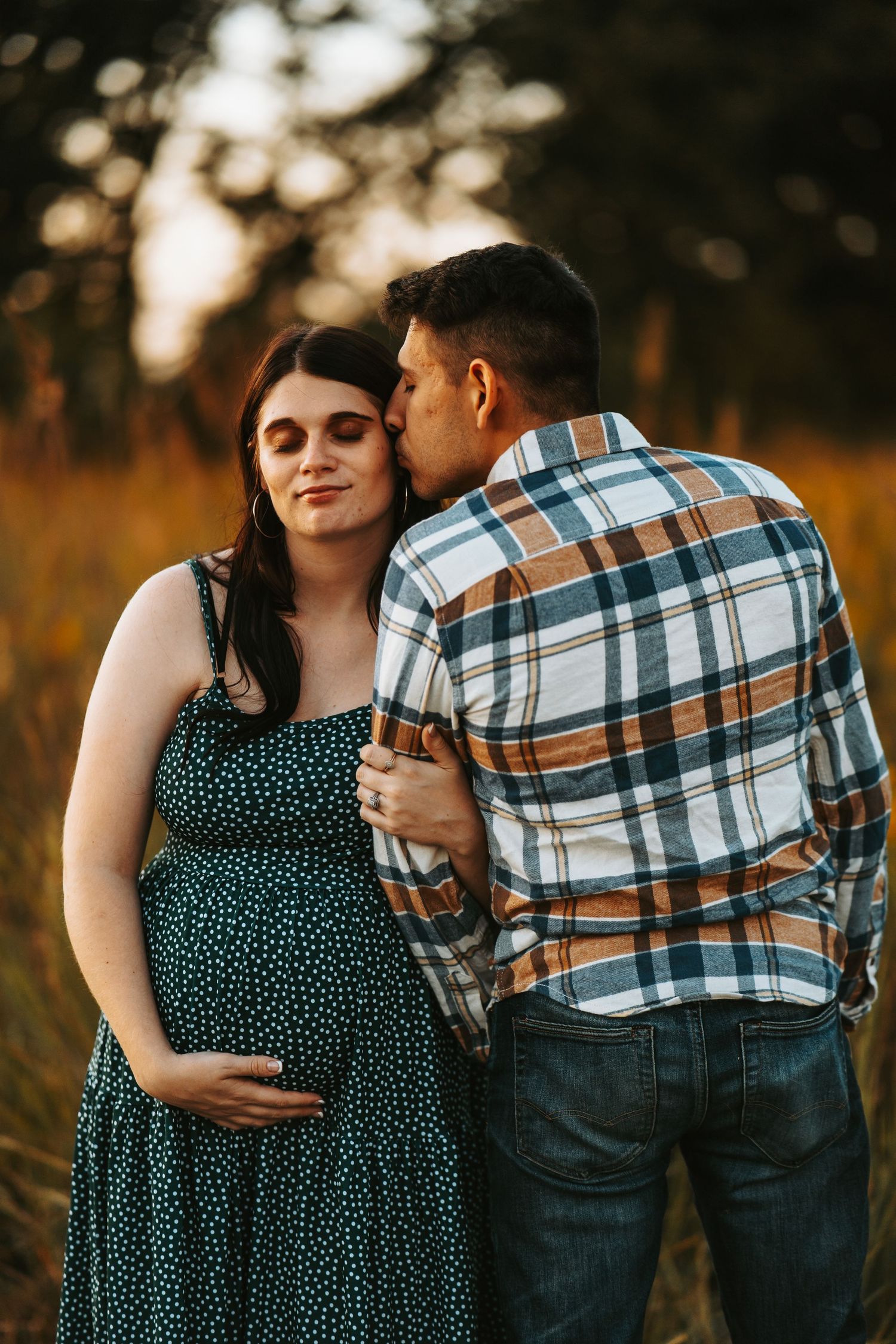A couple in a polka dot dress and plaid shirt embrace during a golden hour outdoor photo session.