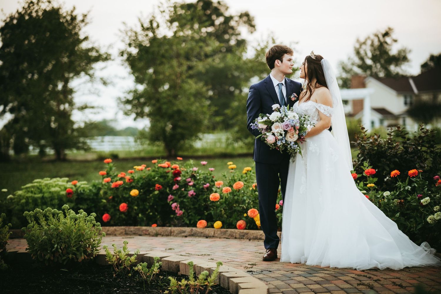 A couple embraces in a beautiful garden setting with red roses and lush greenery on their wedding day.