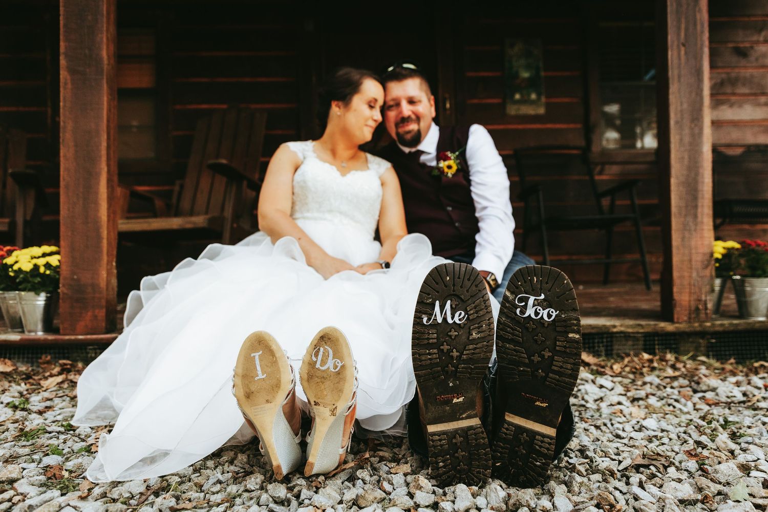 A romantic couple in wedding attire sits together on rustic wooden steps surrounded by fallen autumn leaves.