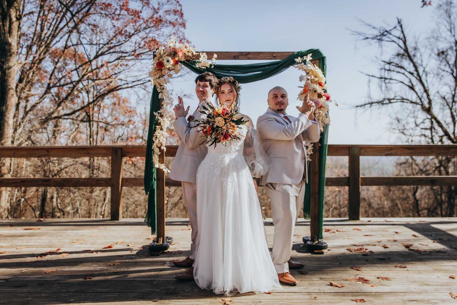 A couple in wedding attire dances together in an outdoor setting surrounded by autumn trees and fallen leaves.