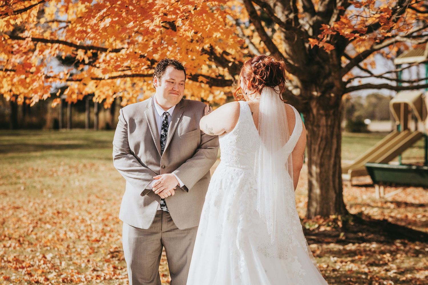 Wedding couple poses under vibrant orange fall trees during outdoor photo session.