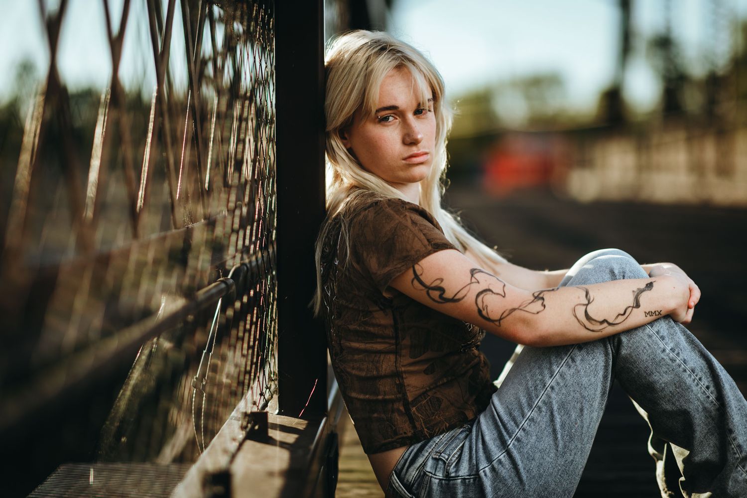 Person sitting on wooden fence at sunset with golden sunlight filtering through trees in rustic outdoor setting.
