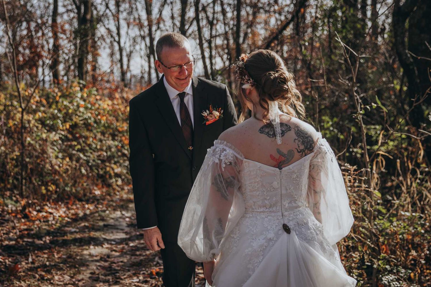 Newlyweds share an intimate moment in a wooded autumn setting with warm sunlight filtering through the trees.