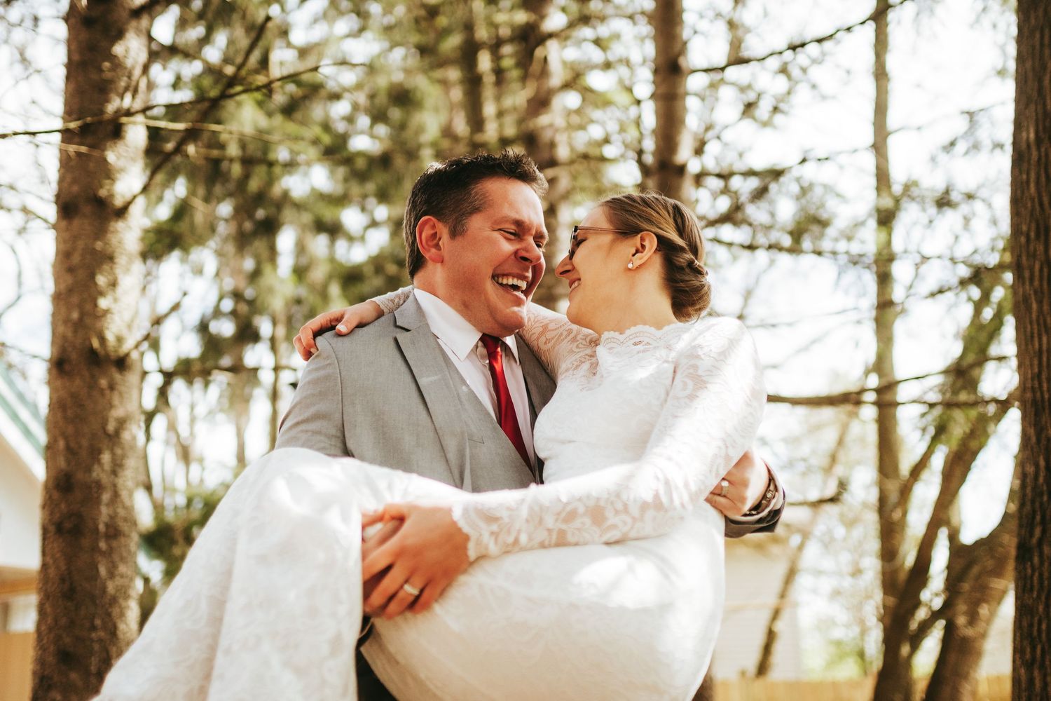 A couple in wedding attire embraces while dancing in a sunlit forest setting.