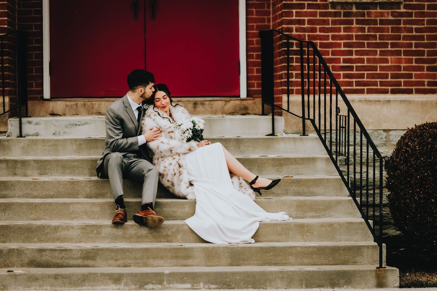 A couple in wedding attire sits intimately on brick steps during their urban photo session.