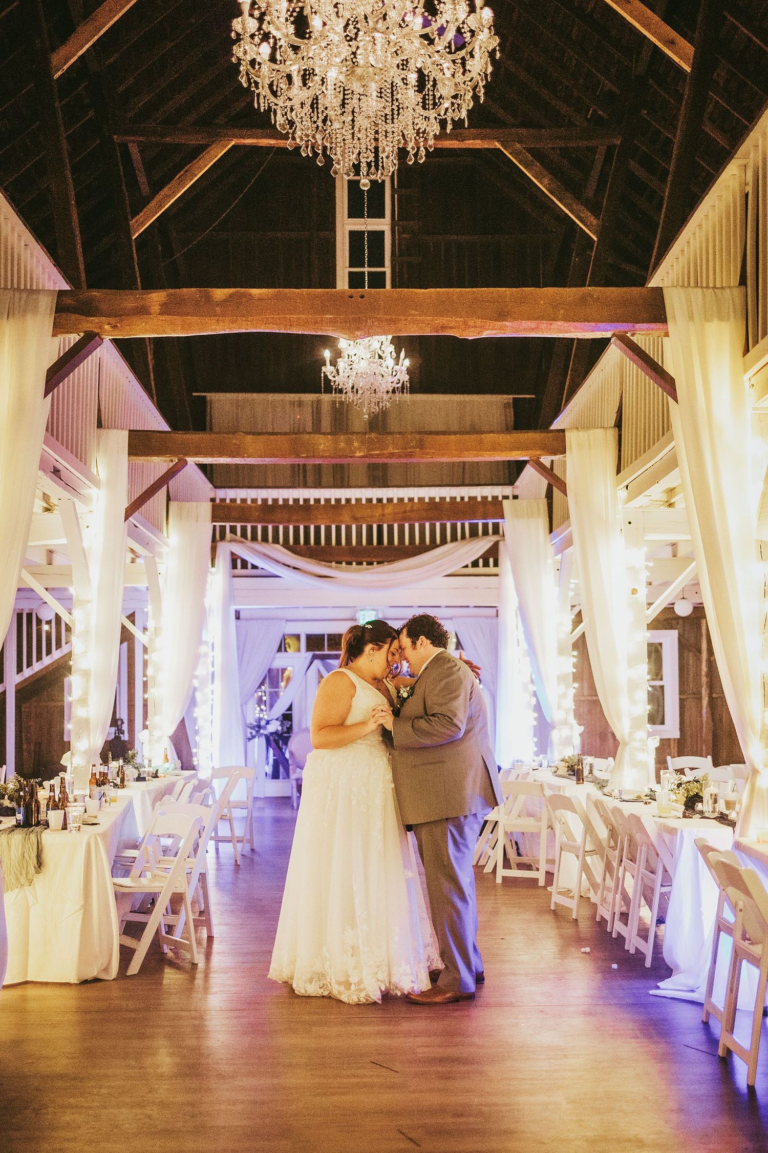 Elegant wedding venue with crystal chandeliers and white draping in a rustic barn setting.