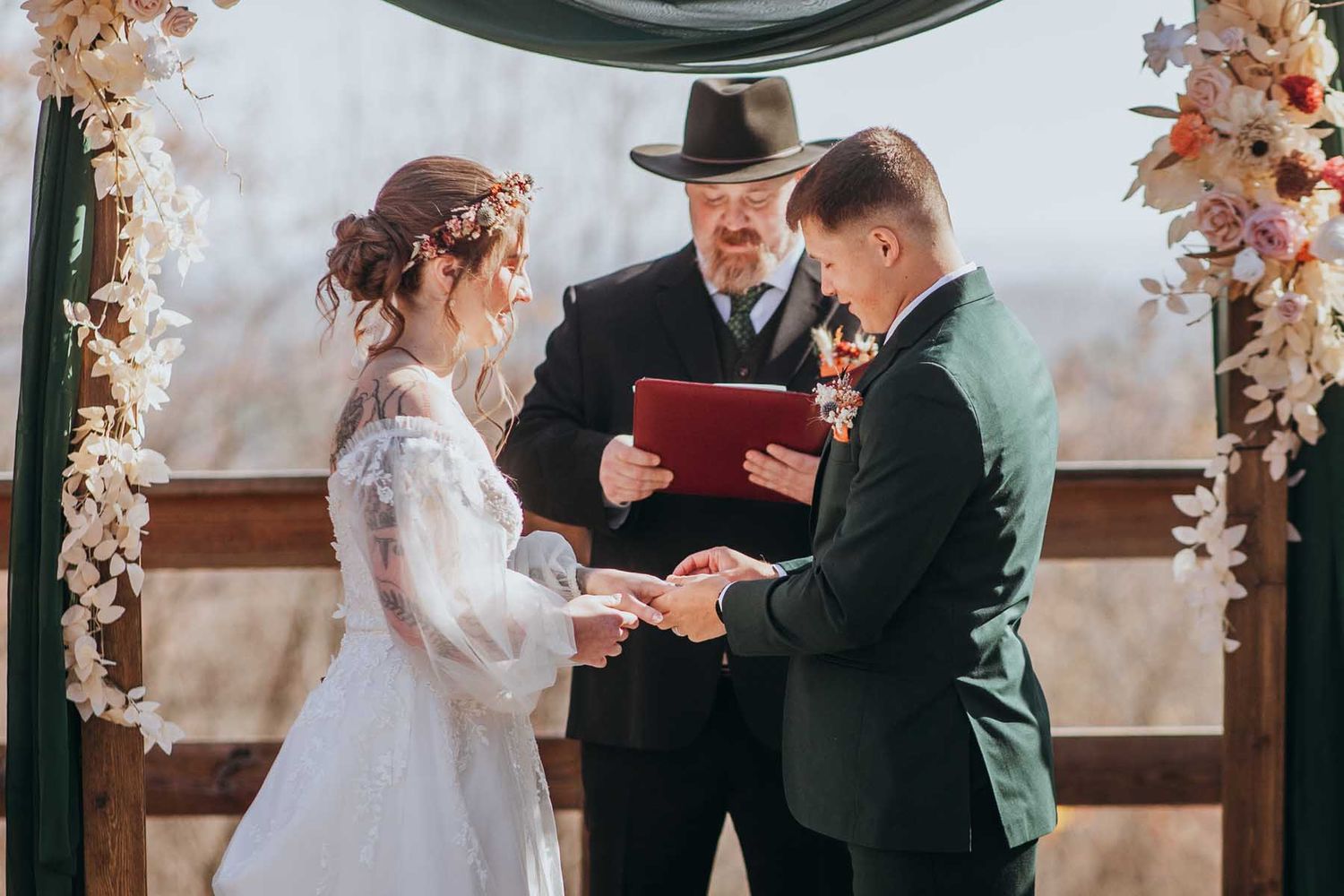 A couple exchanges vows during an autumn wedding ceremony with fall foliage decorations in the background.