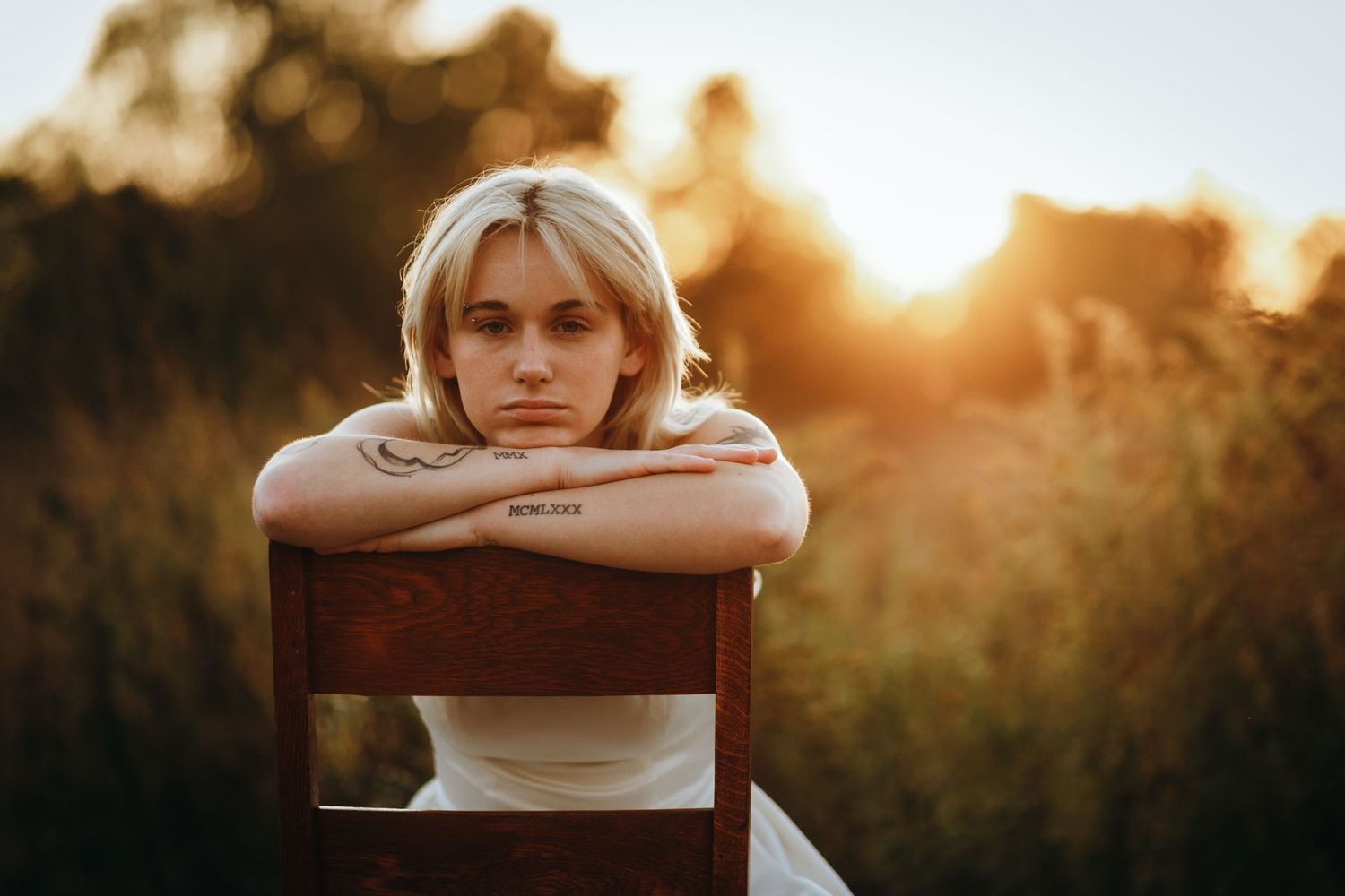 Person resting head on arms against railing during golden sunset in outdoor setting.