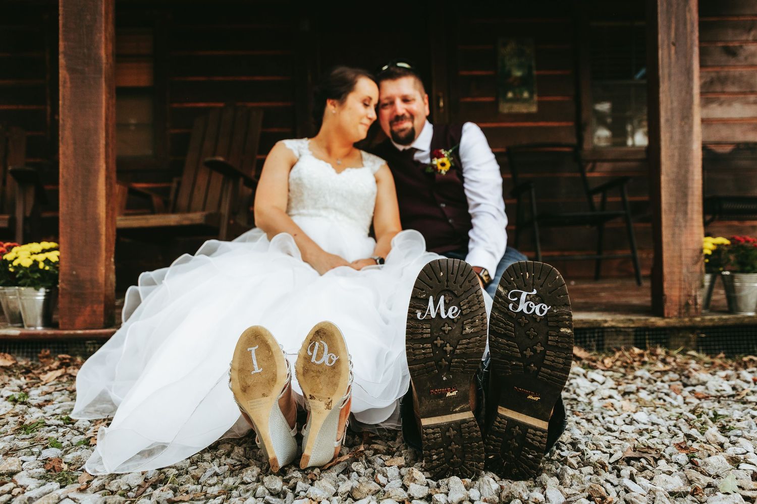 A couple in wedding attire sits together on rustic wooden steps surrounded by autumn leaves.