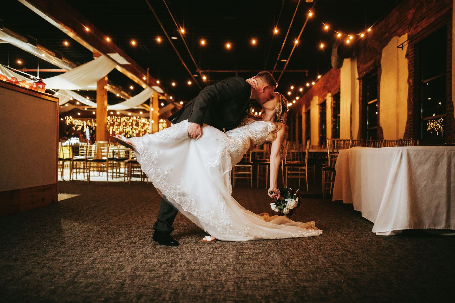 String lights illuminate a romantic dance scene at an elegant indoor wedding reception venue.