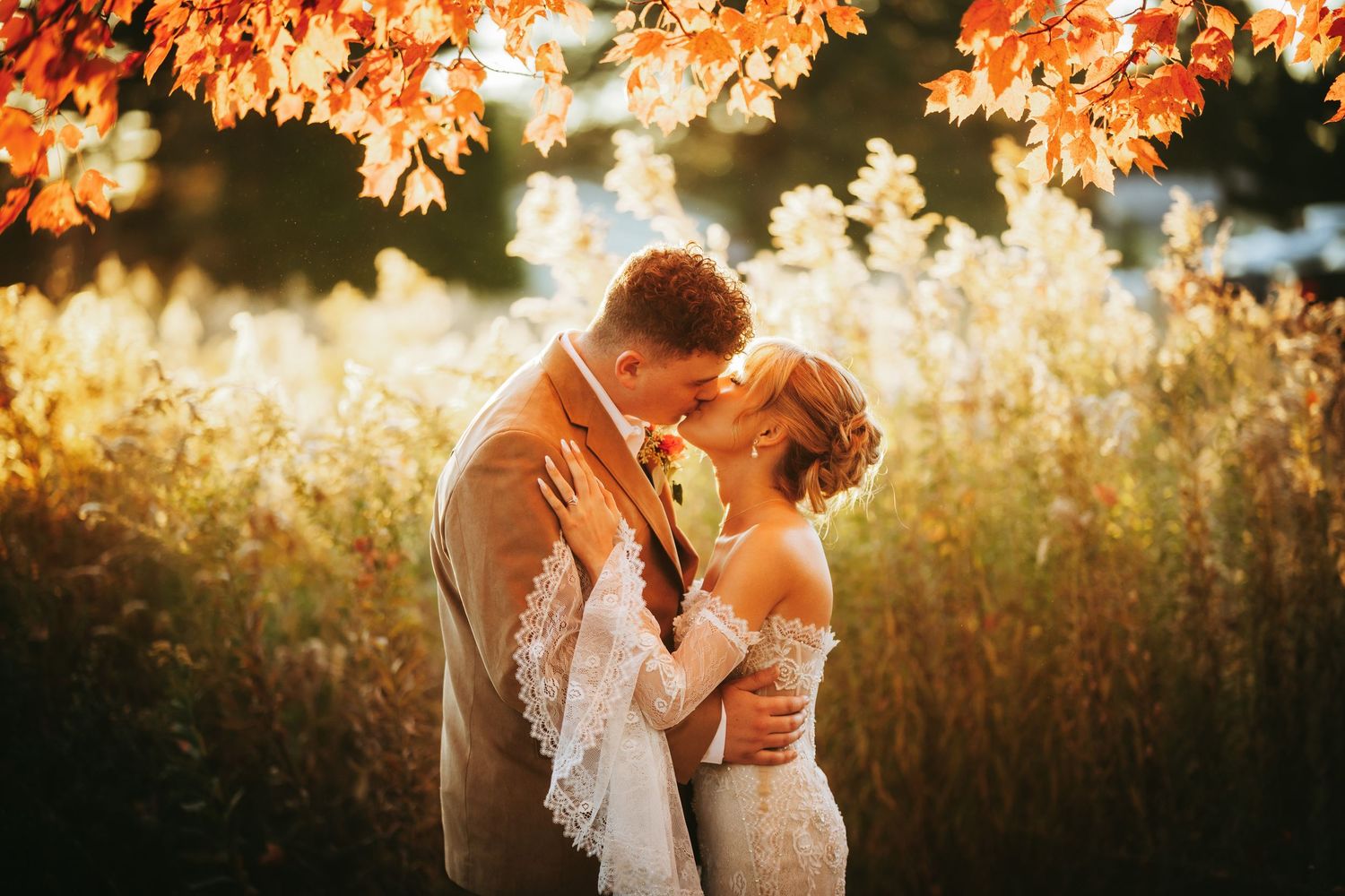 A romantic couple embraces in a golden field at sunset during an intimate outdoor photo session.