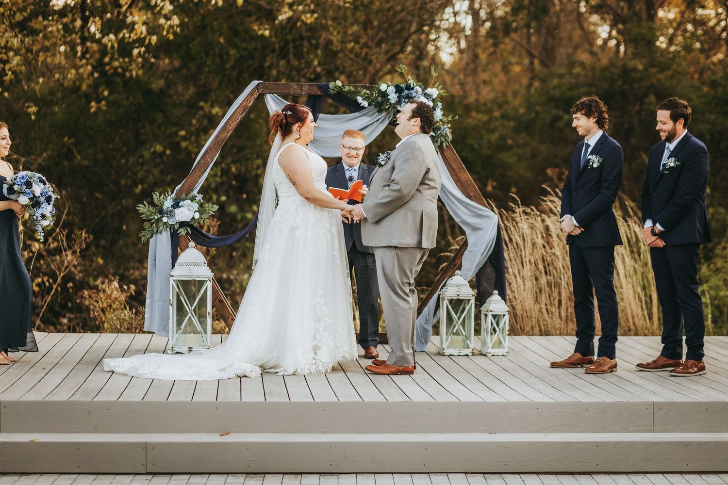Wedding ceremony setup on a wooden deck with white chairs and natural fall scenery in the background.