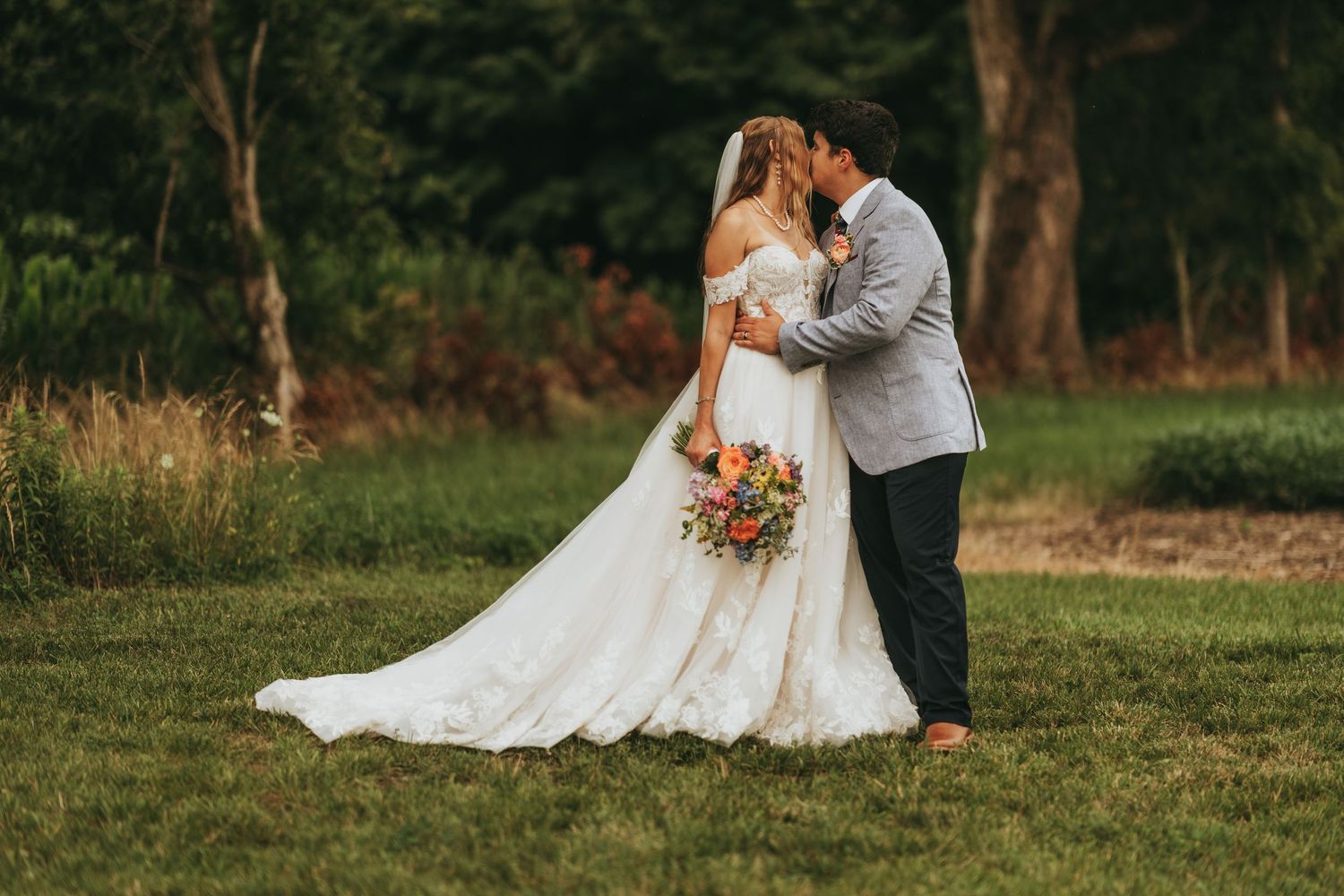 Bride and groom sharing a romantic kiss on a lush green lawn on their wedding day.