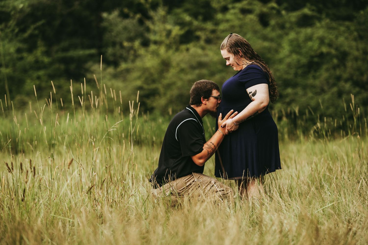 A couple shares an intimate moment together while standing in a tall grass meadow on a sunny afternoon.