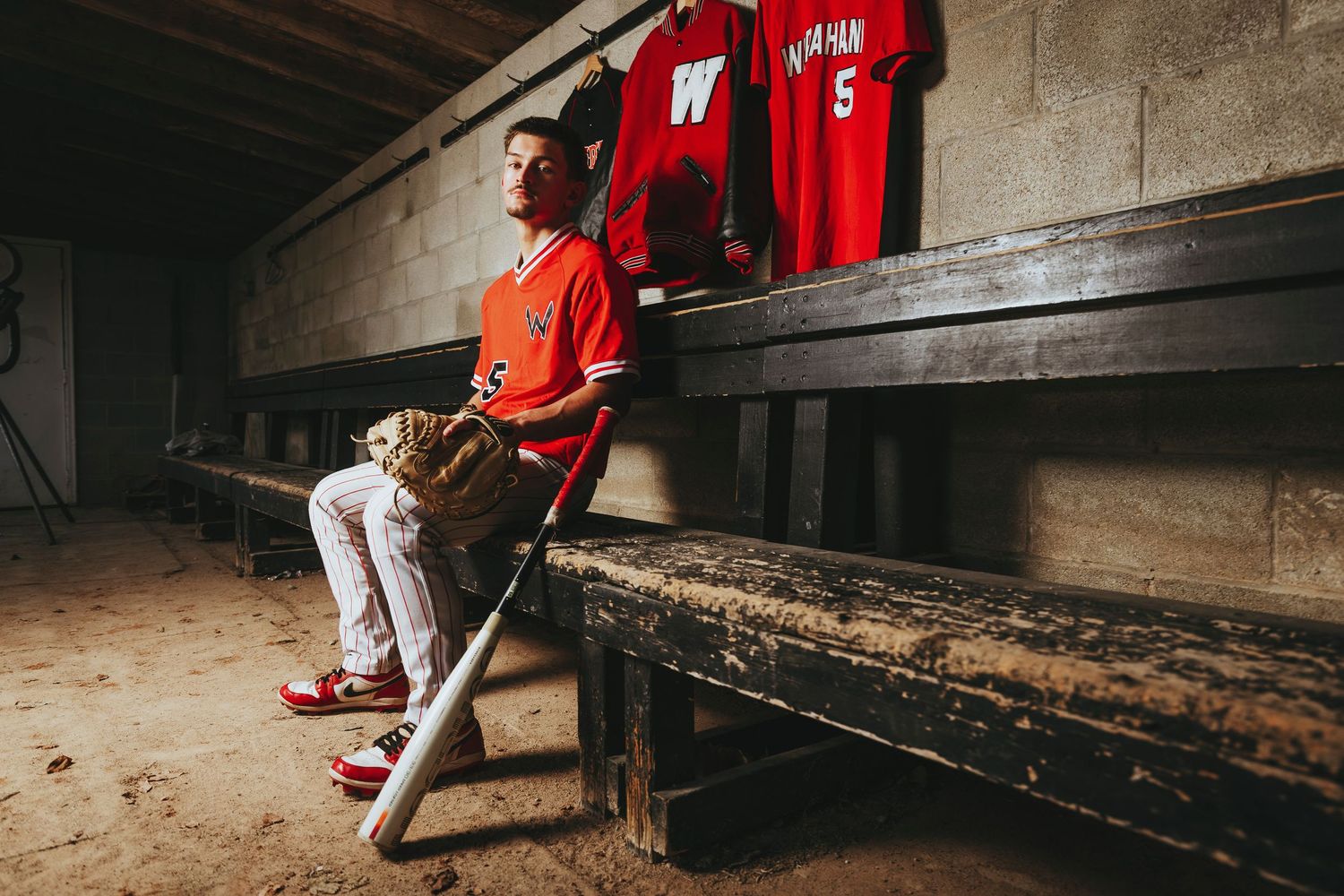 Baseball player in red uniform sits on dugout bench while waiting for game to start.