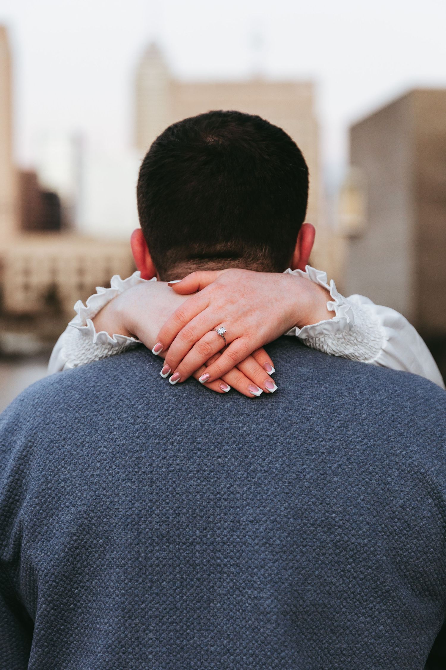 A close-up view of hands with painted nails embracing around someone's neck wearing a gray sweater.