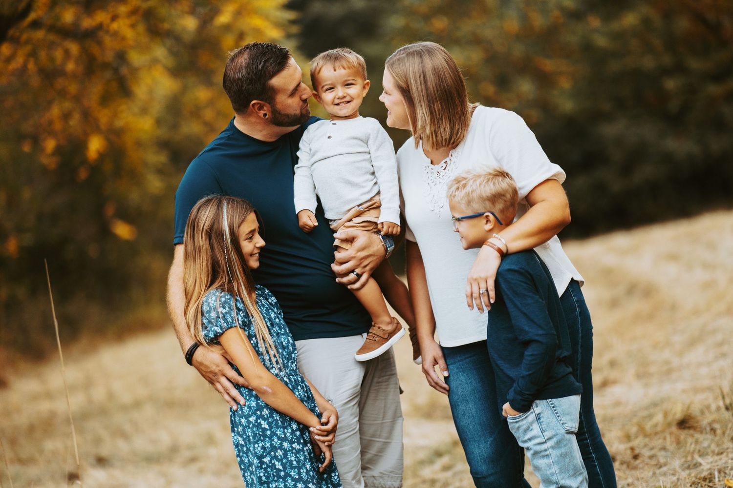 A family shares tender moments together on a sunny autumn hillside in coordinated blue and white outfits.