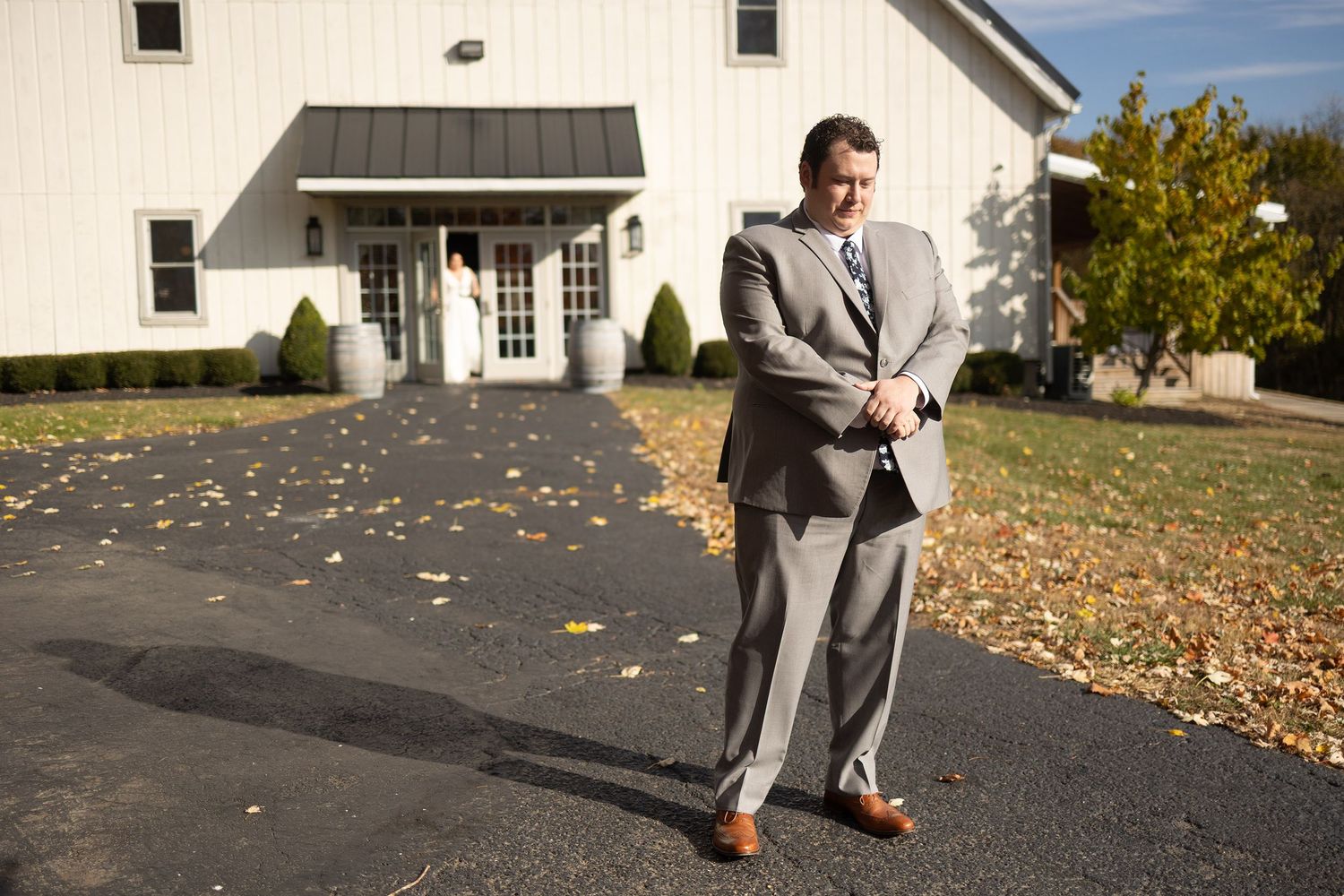 Wedding portraits taken on path with fallen leaves near white building.