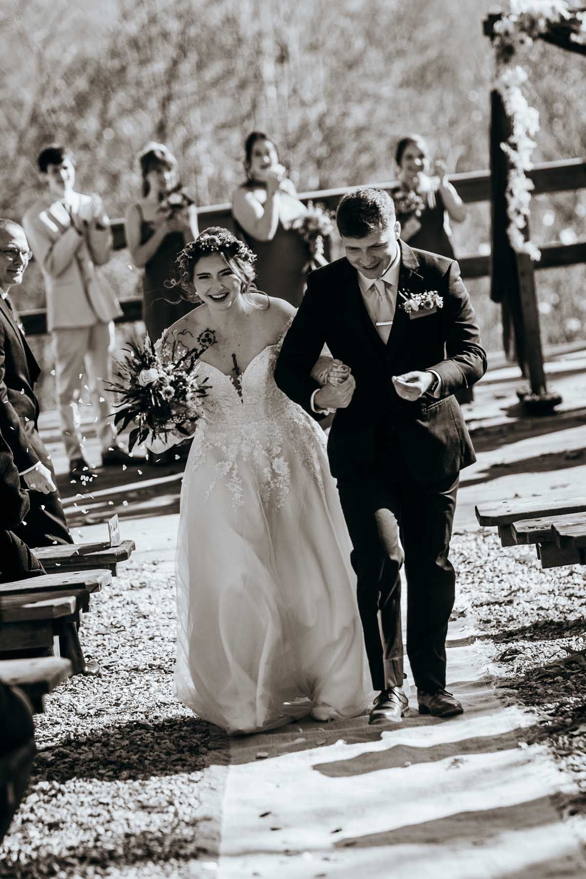 Black and white wedding photos capturing a couple walking together on a leaf-covered pathway.