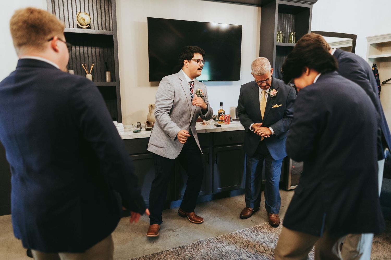 Men in suits socializing in a modern room, one gesturing while others laugh during a formal gathering.