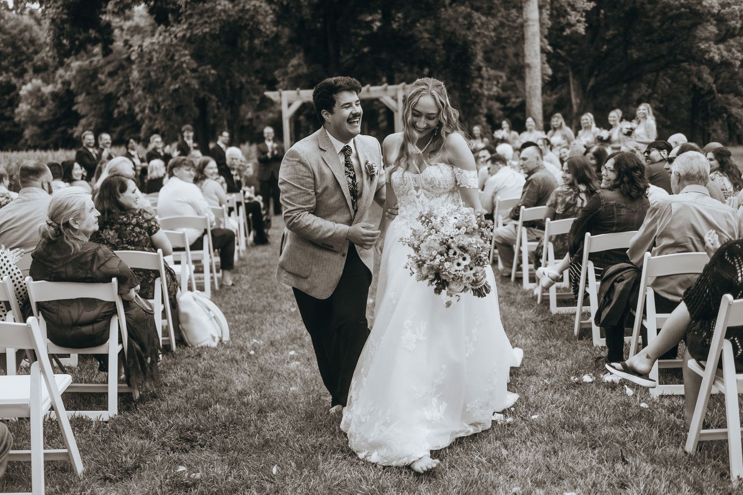 Black and white photo of a newlywed couple walking down the aisle after their outdoor wedding ceremony.