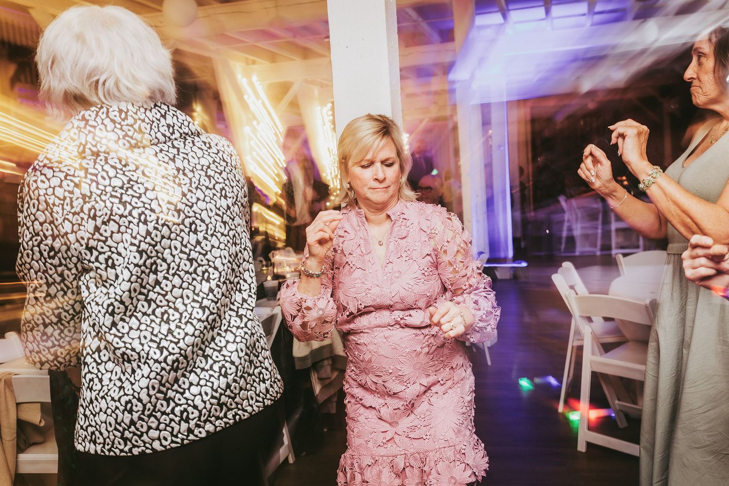 Wedding guests dancing and celebrating on a dance floor illuminated by purple and pink lighting.