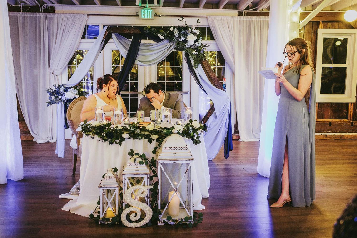 Wedding reception hall decorated with white draping and purple uplighting creating an elegant atmosphere.