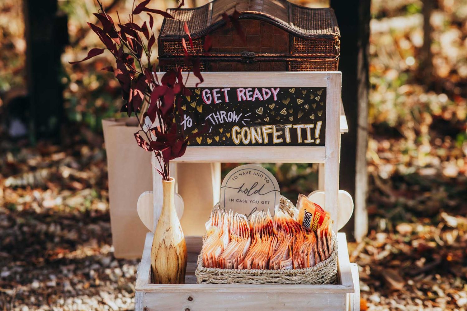 Rustic outdoor fall wedding decor features wooden signs, candles, and autumn leaves scattered on the ground.
