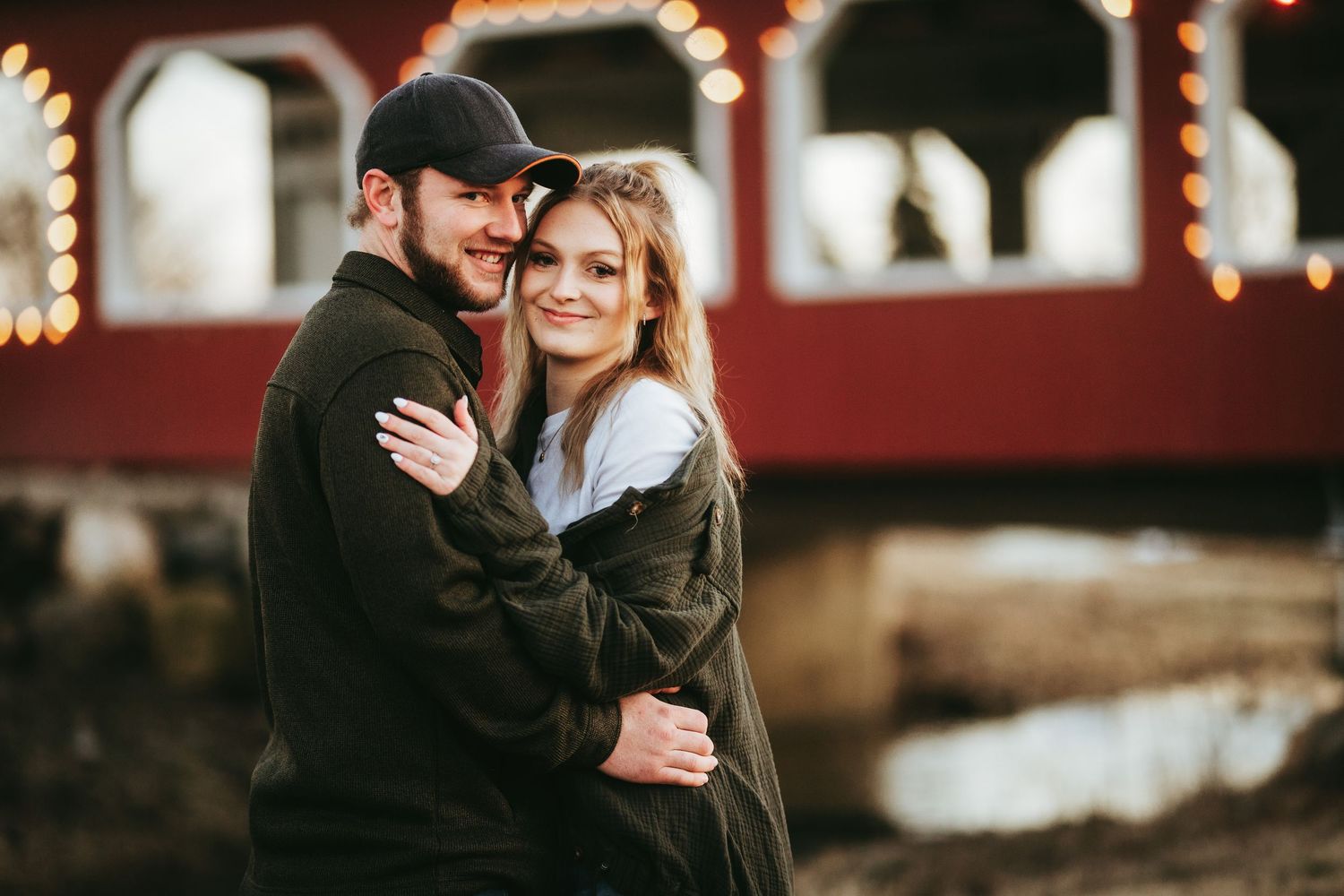A couple shares a romantic moment under twinkling lights at dusk in a cozy outdoor setting.
