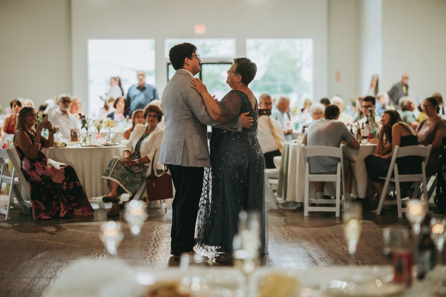 Couple sharing intimate dance on wooden floor surrounded by guests at elegant wedding reception.