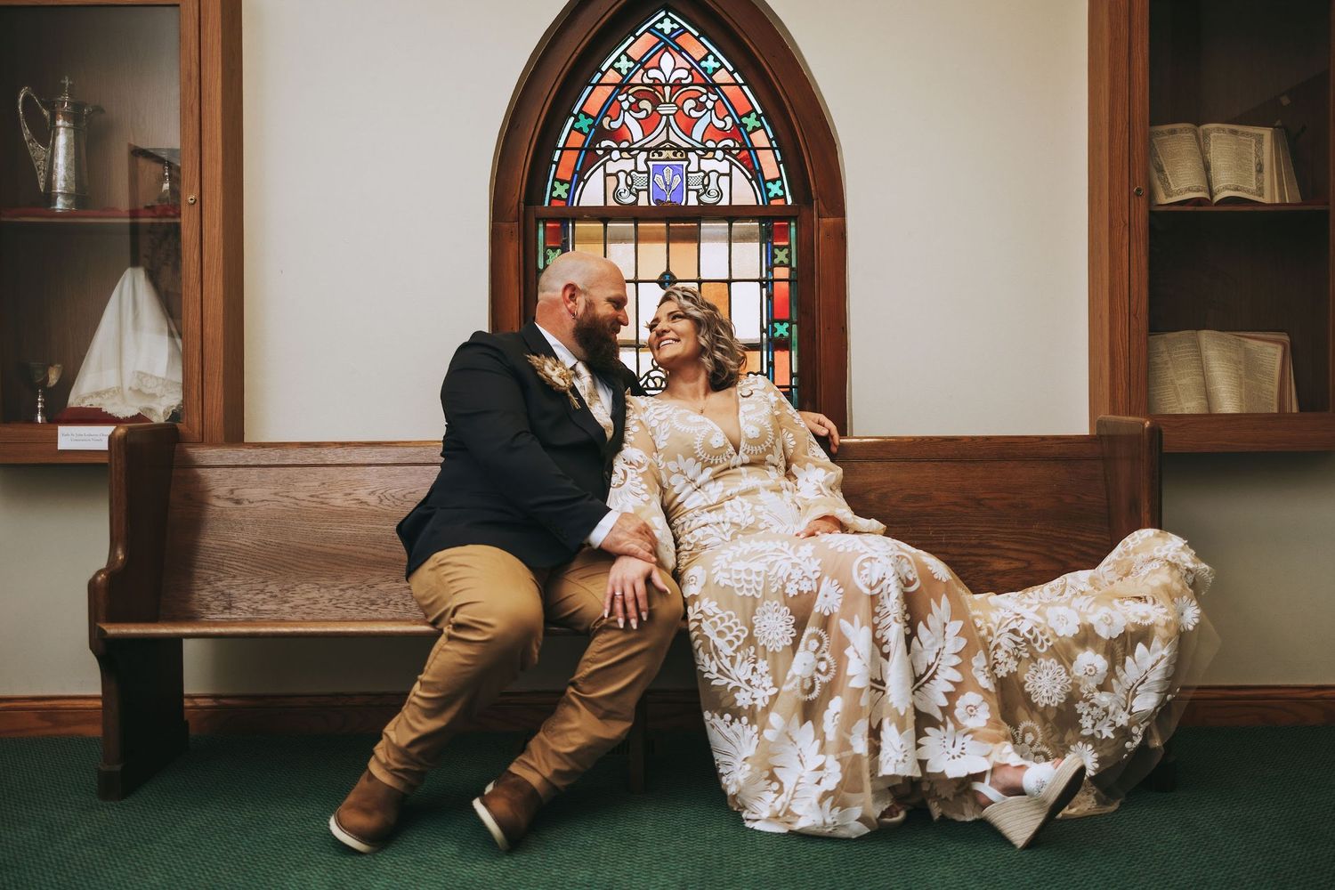 Two people sit on the floor of a church or chapel with a stained glass window in the background.