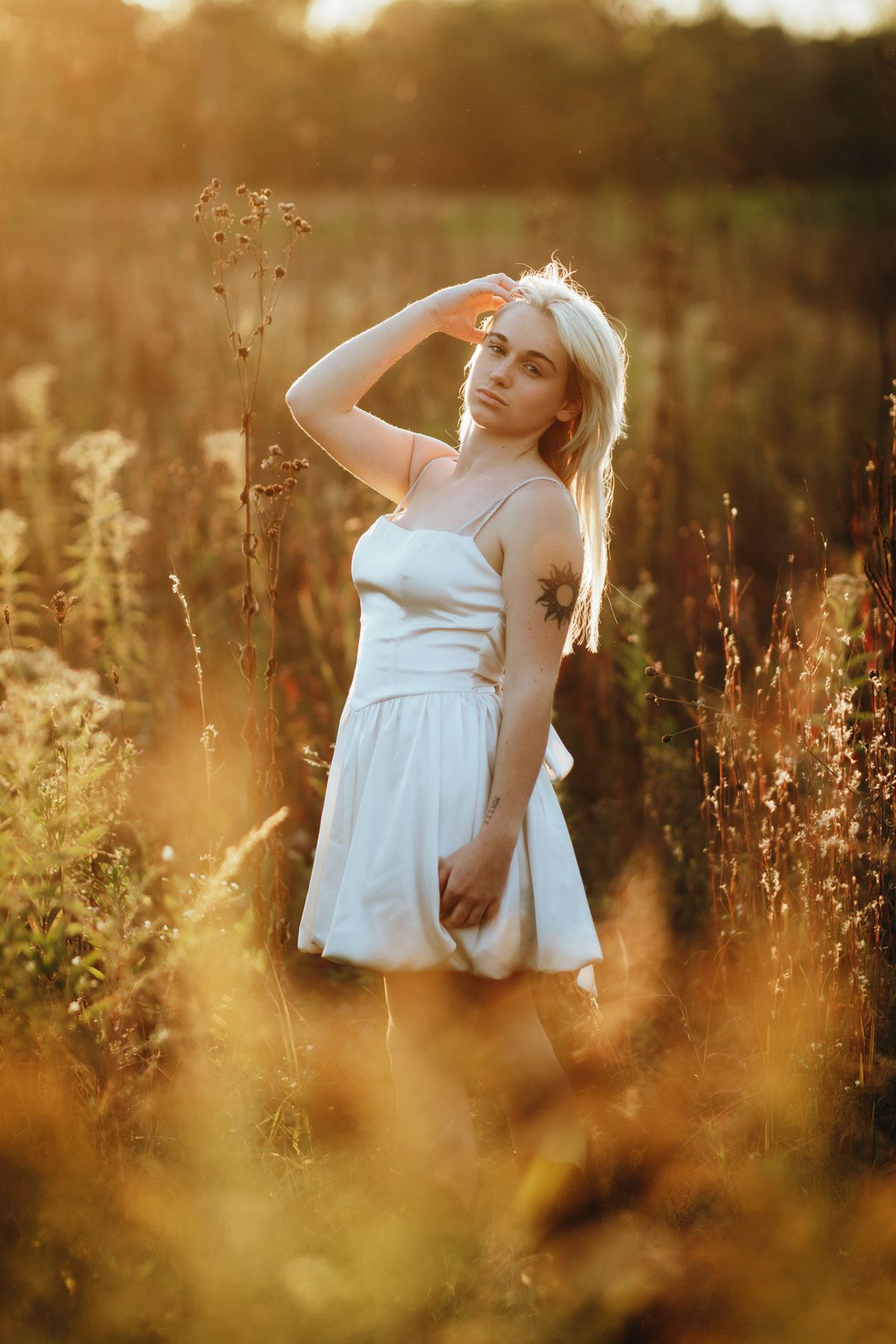 A dreamy sunset portrait in a wildflower meadow shows a white summer dress glowing in golden hour light.