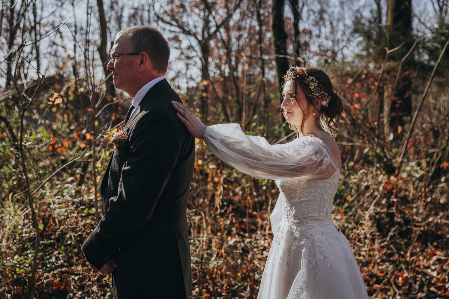A couple shares a romantic dance in a wooded outdoor setting with autumn foliage in the background.