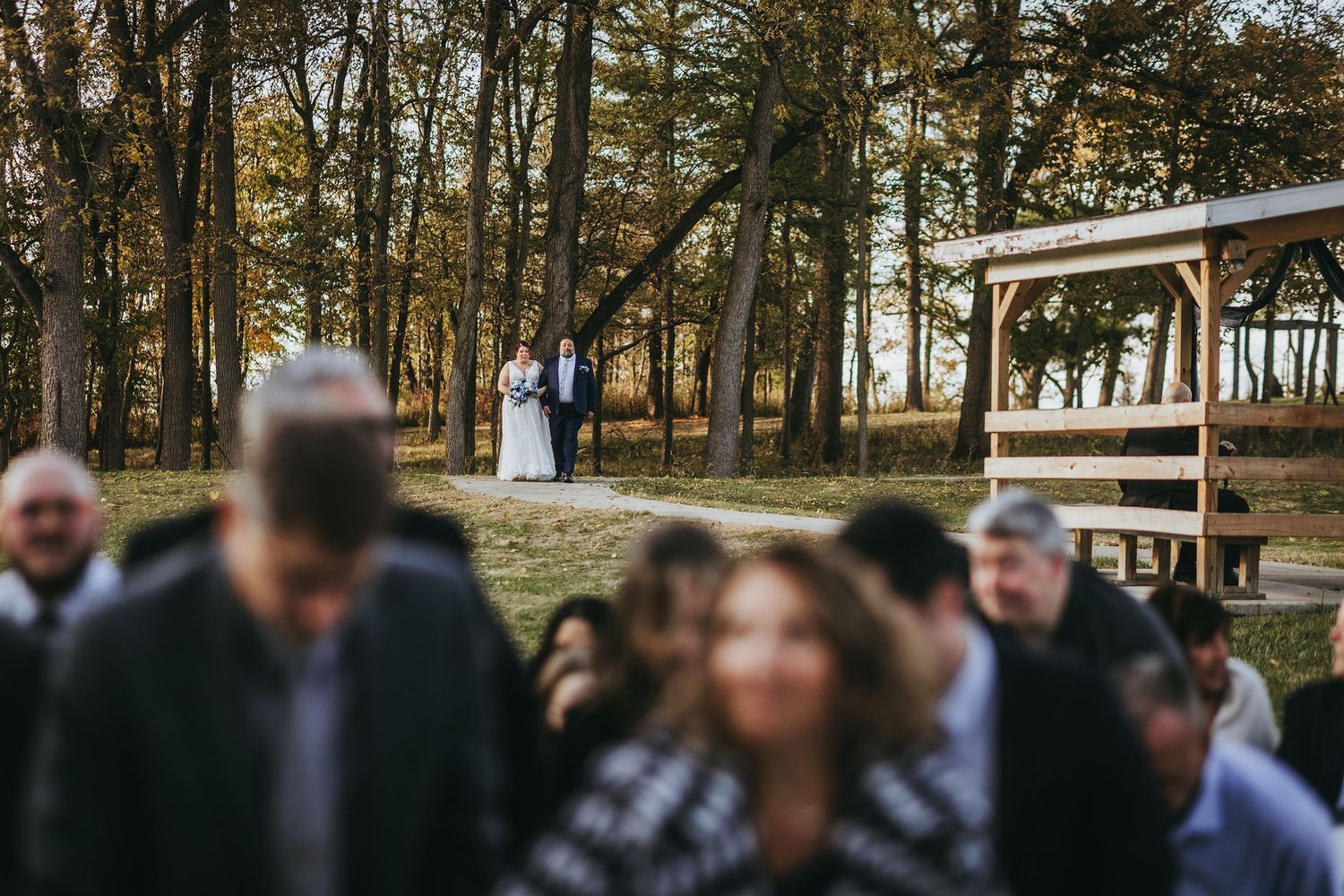 Wedding party members walking outdoors along a wooden deck surrounded by fall foliage.