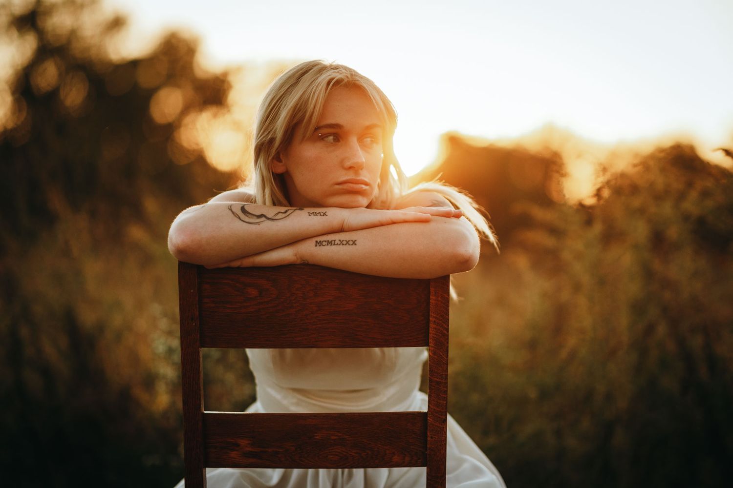 Minimalist outdoor portrait session featuring rustic wooden furniture against a bright white backdrop.