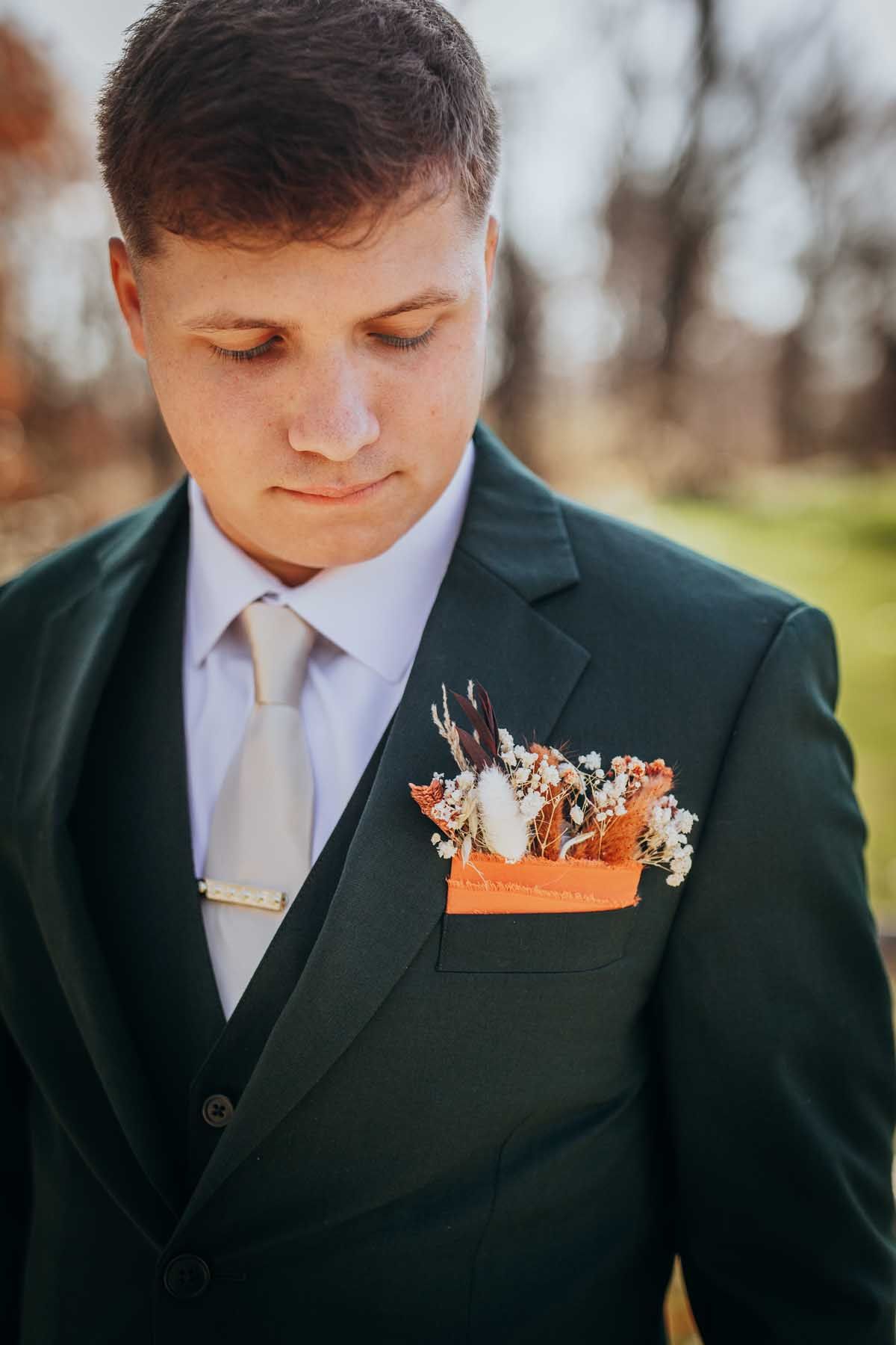 Close up of wedding attire showing a dark green suit jacket with orange and white floral boutonniere.