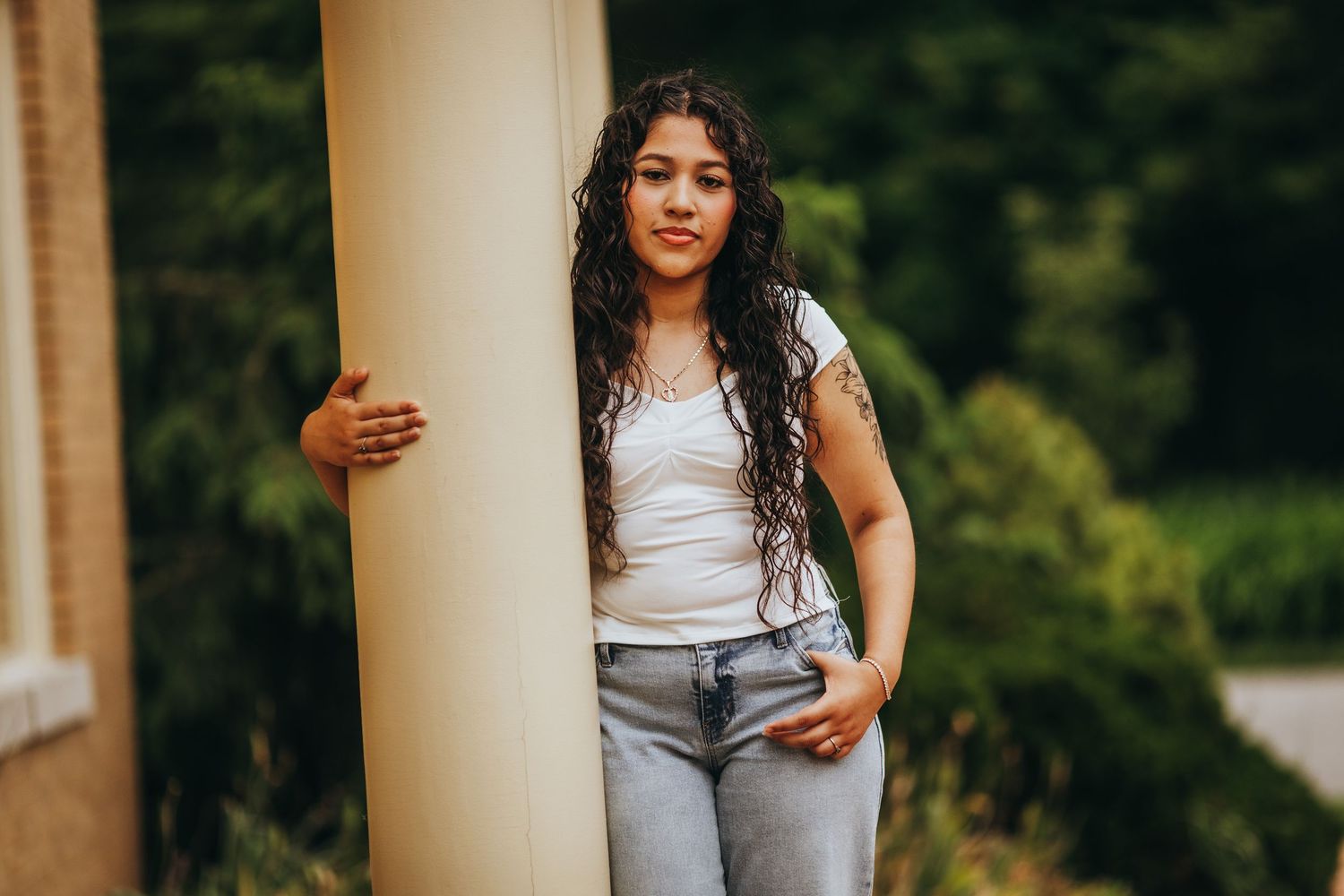 Woman in white tank top and gray pants poses between pillars during golden hour outdoor photoshoot.