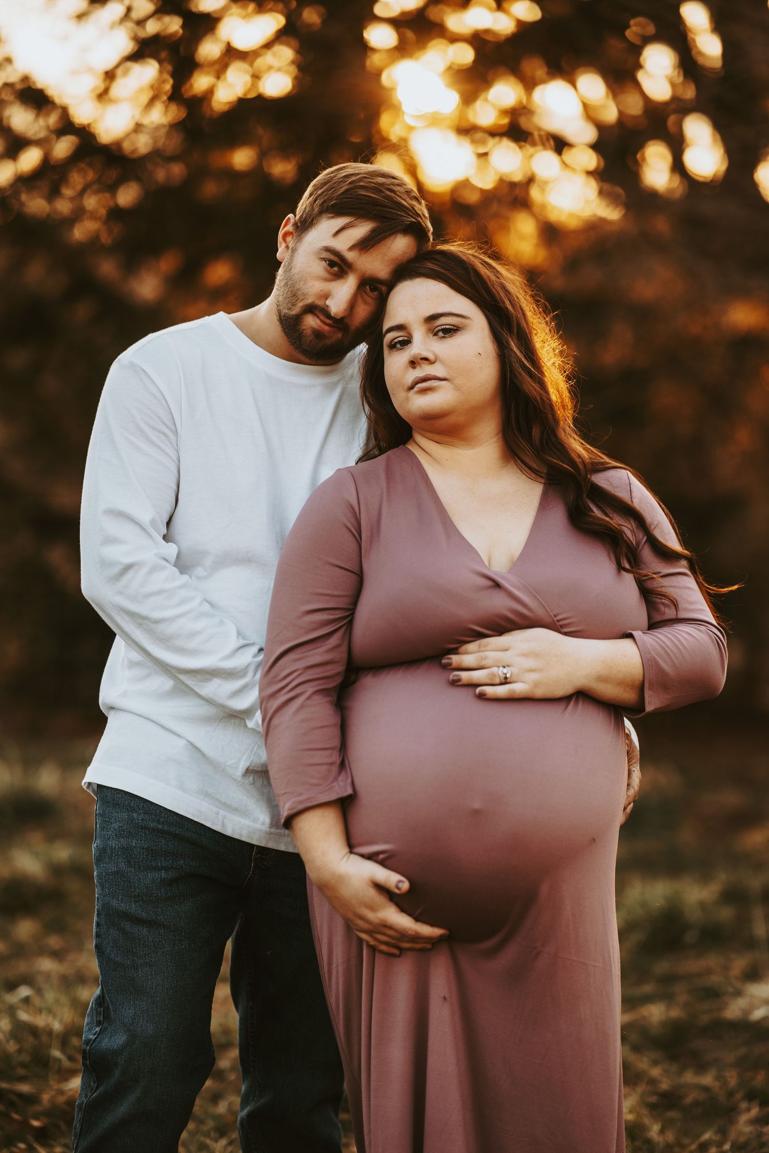 Romantic maternity photoshoot at sunset with couple embracing in warm autumn light.