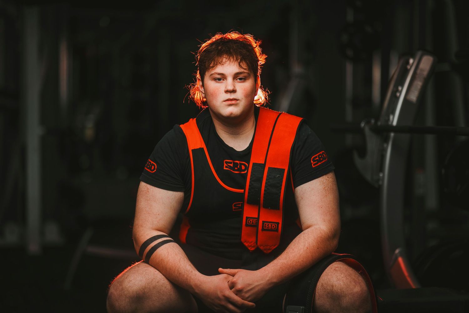 High school football player in black and orange uniform poses for sports portrait against dark background.