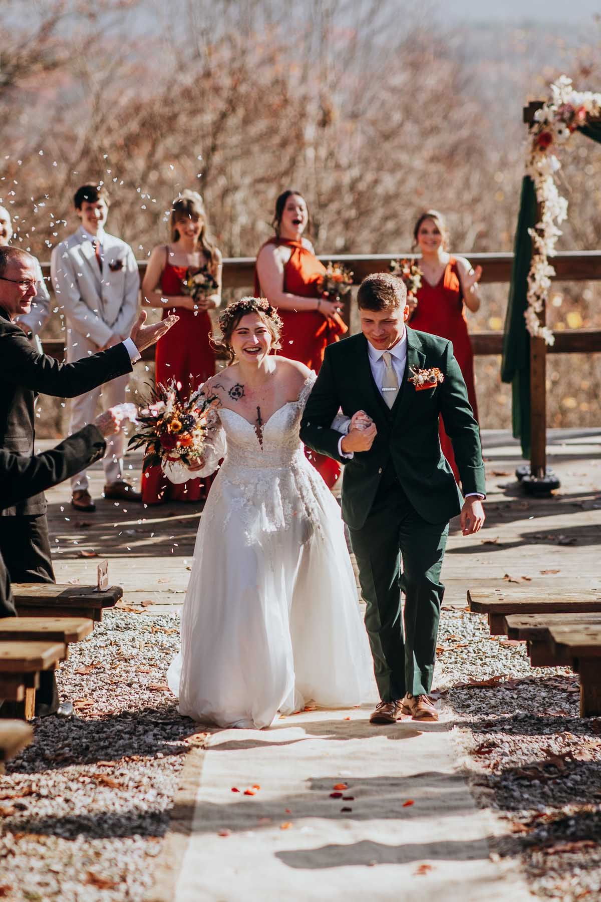 A joyful wedding recessional with bridesmaids in red dresses celebrating on a wooden deck outdoors.