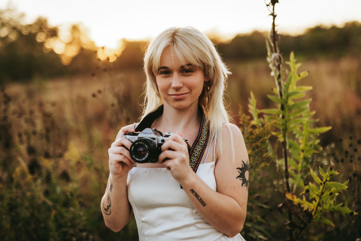 A photographer captures sunset portraits in a golden field with tall grass and wildflowers during magic hour.