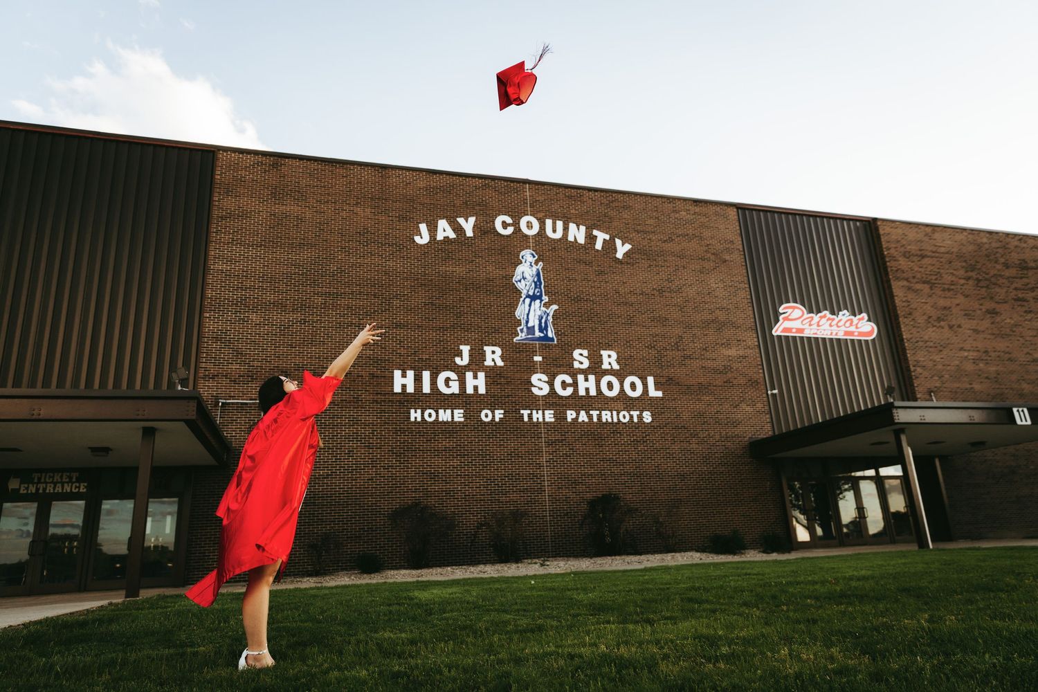 Red graduation cap tossed into the air against a school building backdrop.