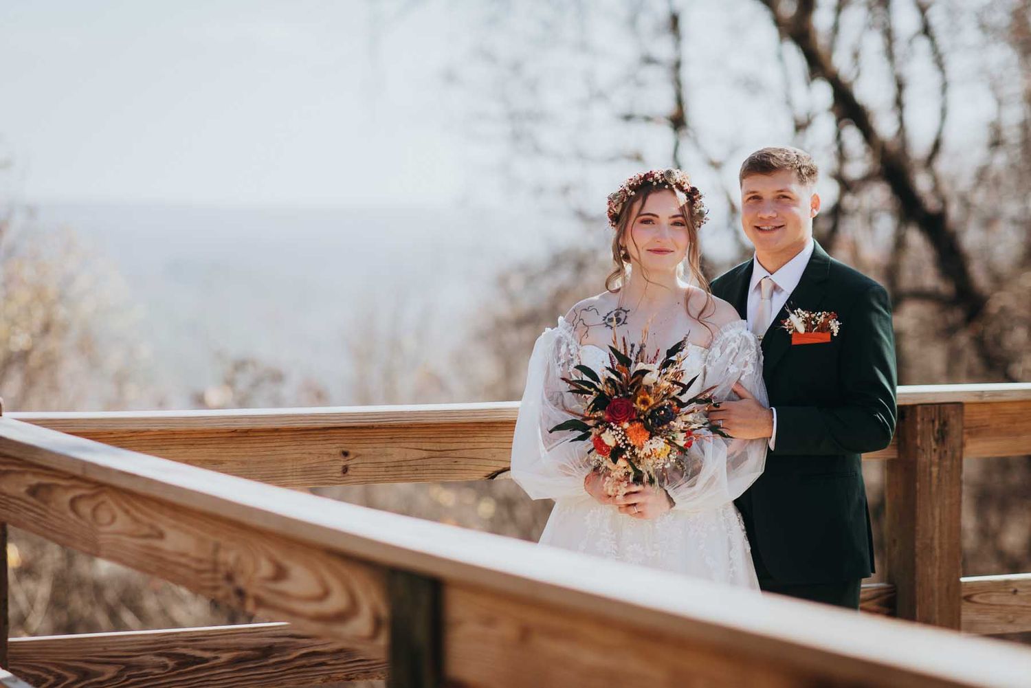 Couple embraces on wooden deck during autumn wedding ceremony with rustic outdoor decor.